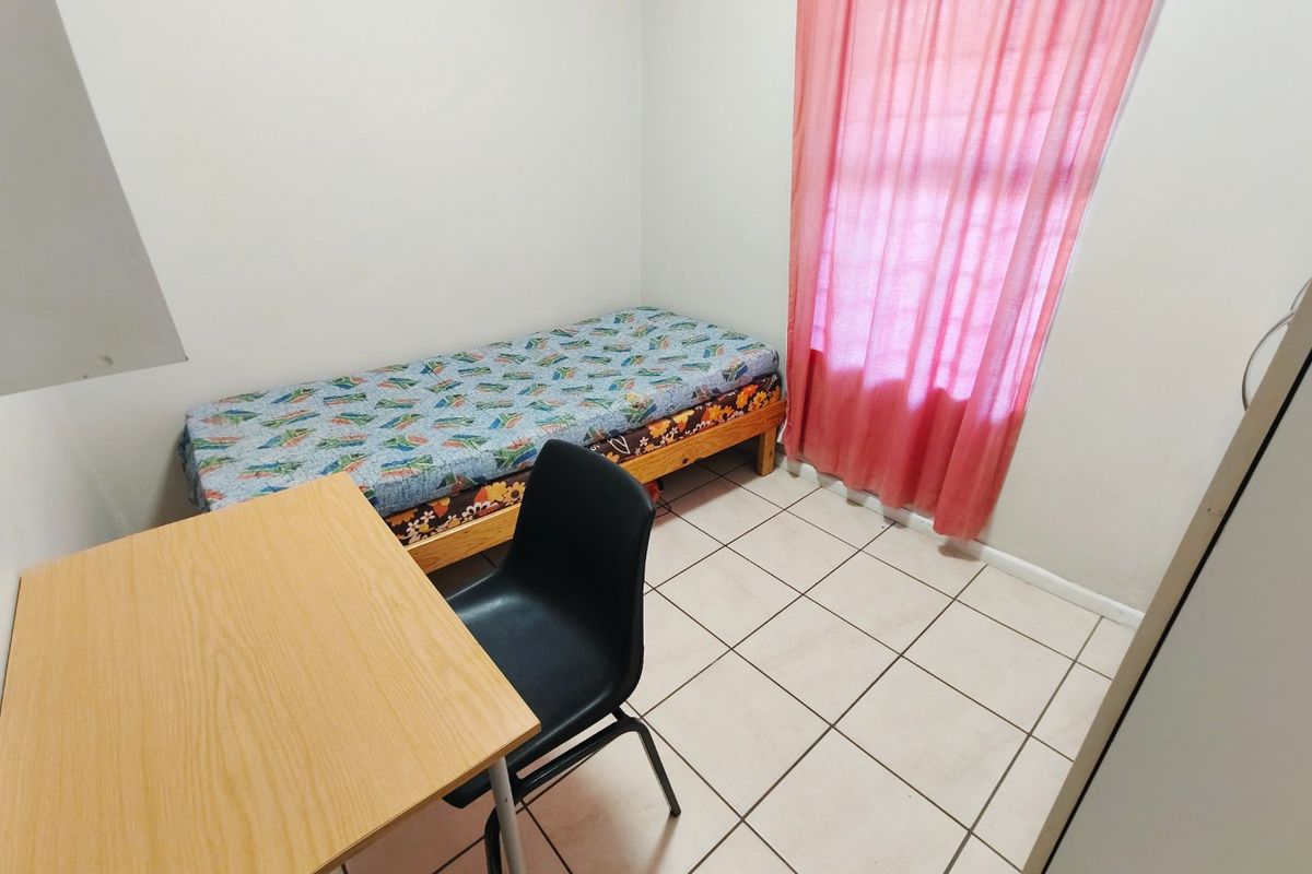 A compact bedroom featuring tiled flooring and a window with curtains.