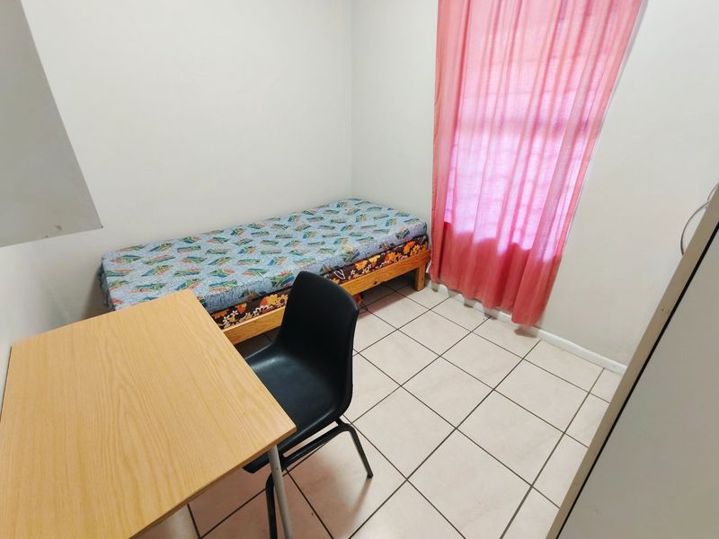 A compact bedroom featuring tiled flooring and a window with curtains.