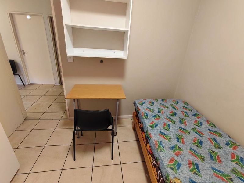A compact bedroom featuring tiled flooring and built-in wall shelving, providing a functional space for a single occupant.