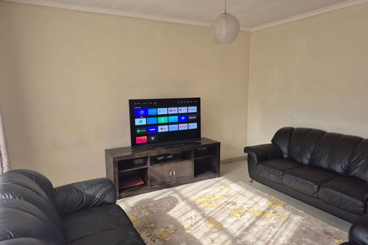 A living room featuring tiled flooring and a central pendant light fixture, with walls showing signs of wear and discoloration.