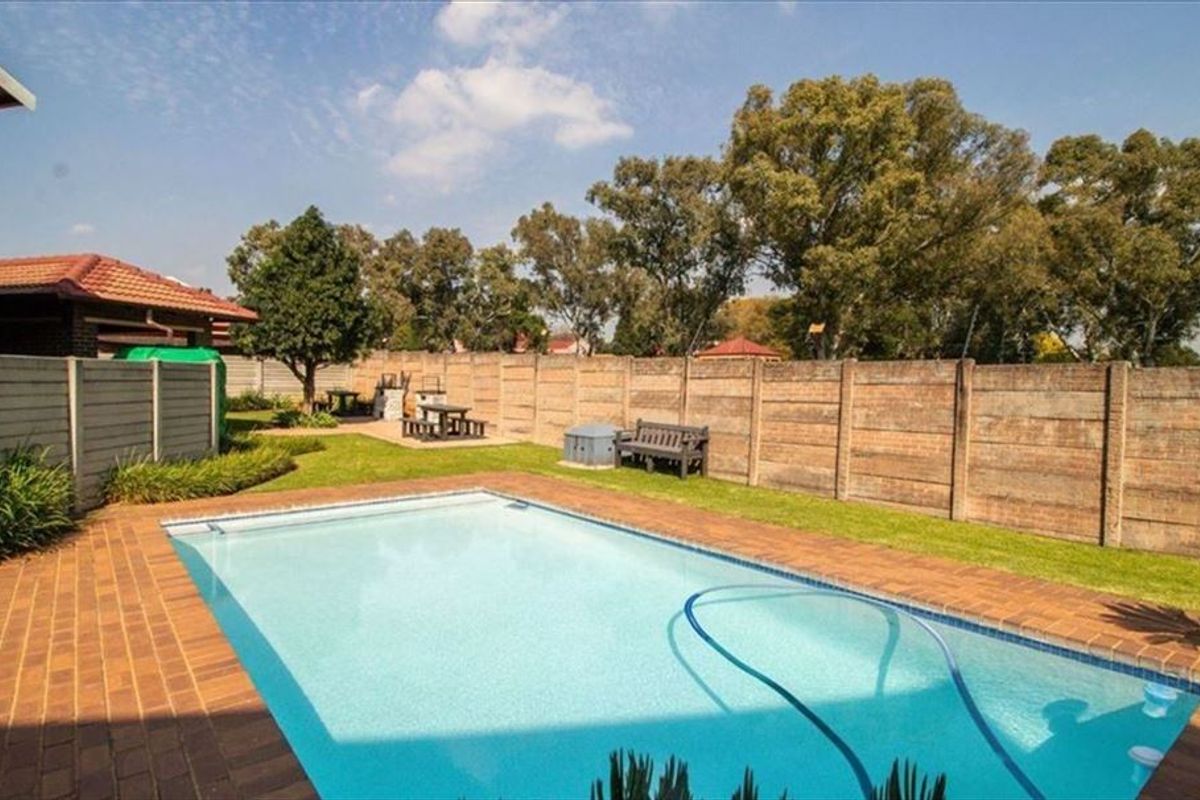 A private backyard featuring a swimming pool with brick coping, surrounded by a lawn and enclosed by a precast concrete boundary wall.