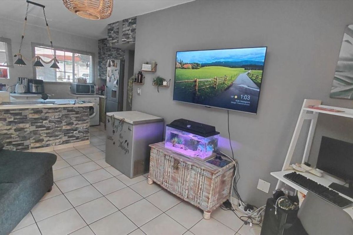 Open-plan living area featuring tiled flooring and a kitchen with a breakfast bar finished in stone-look cladding.