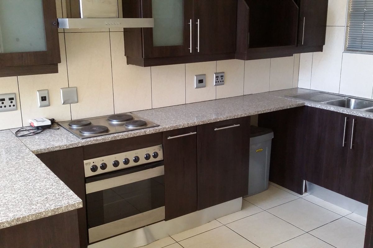 A functional kitchen featuring dark wood cabinetry, granite countertops, a built-in oven with electric hob, and a stainless steel sink with tiled backsplash.