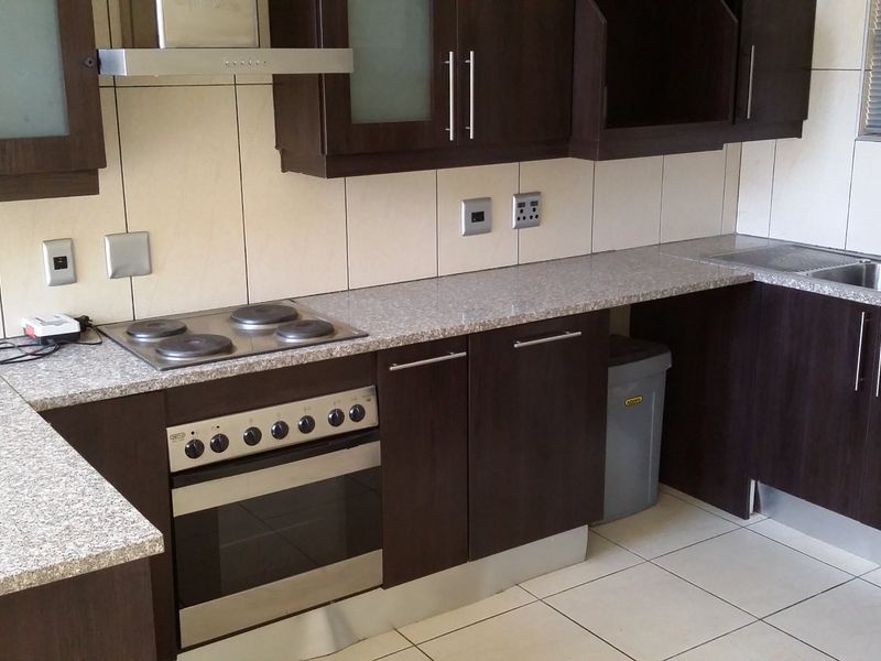 A functional kitchen featuring dark wood cabinetry, granite countertops, a built-in oven with electric hob, and a stainless steel sink with tiled backsplash.