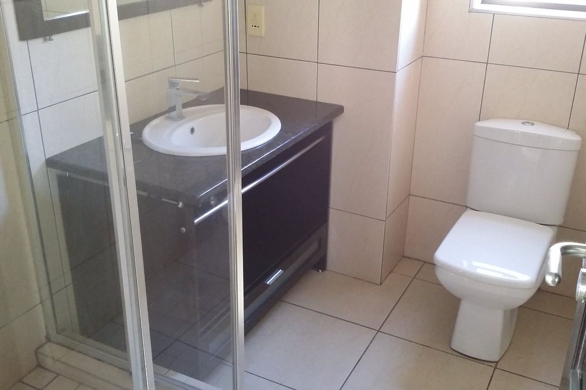 A clean, functional bathroom featuring a modern vanity with granite countertop, a glass-enclosed shower, and neutral ceramic tiling throughout.