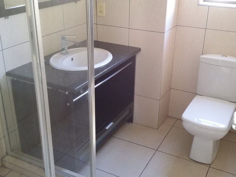 A clean, functional bathroom featuring a modern vanity with granite countertop, a glass-enclosed shower, and neutral ceramic tiling throughout.