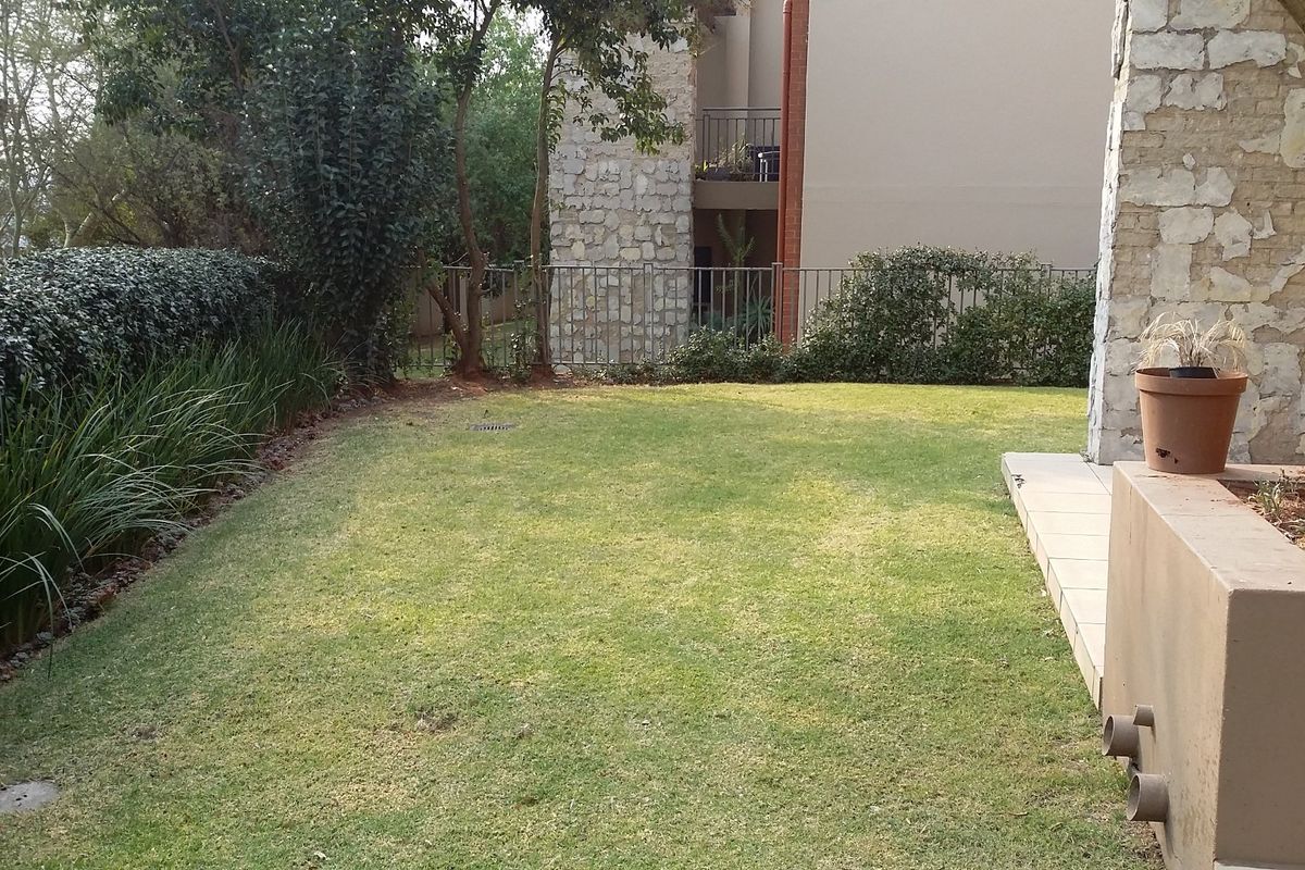 A private rear garden area featuring a manicured lawn, stone-clad structural elements, and perimeter metal fencing.