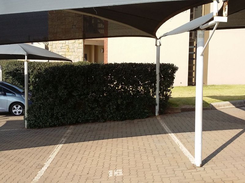 Outdoor parking area featuring covered shade cloth carports with paved bays and established hedge landscaping.