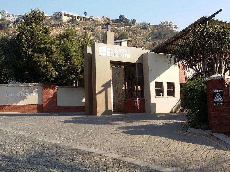 The main entrance and security gatehouse of the apartment complex, featuring paved access, brick boundary walls, and integrated security infrastructure.