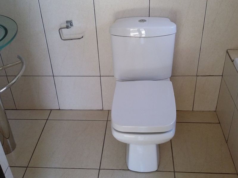 A functional bathroom featuring a white toilet, a glass pedestal washbasin, and a built-in bathtub with neutral ceramic wall and floor tiling.