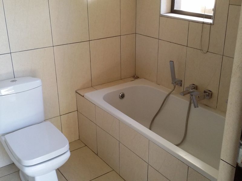 A functional bathroom featuring a built-in bathtub with handheld shower attachment, a standard toilet, and neutral wall and floor tiling.