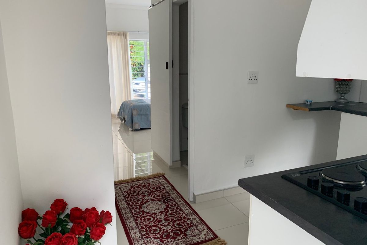 A view from the kitchen area looking through a sliding door towards a bedroom, featuring tiled floors and a built-in hob with extractor.