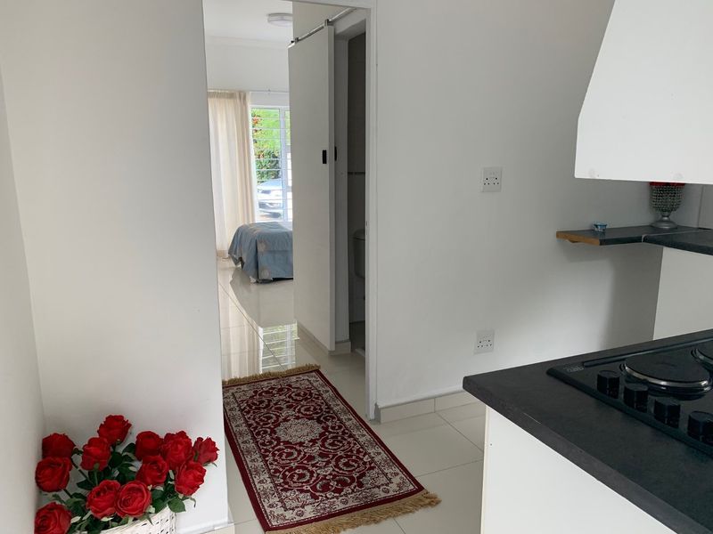 A view from the kitchen area looking through a sliding door towards a bedroom, featuring tiled floors and a built-in hob with extractor.