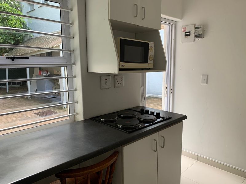 Compact kitchen area featuring built-in cabinetry, an electric hob, and a built-in microwave, with direct access to an outdoor patio area.