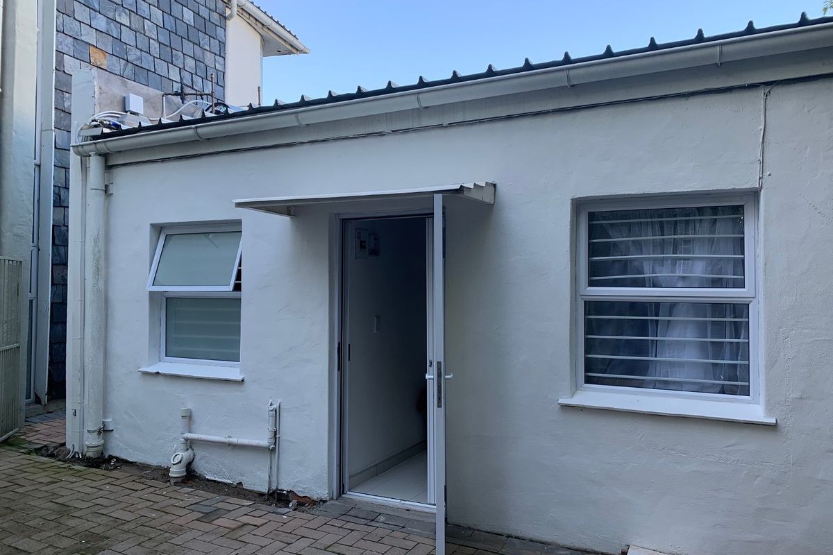 Rear exterior view of the apartment featuring a paved patio area, white rendered walls, and security-fitted windows.