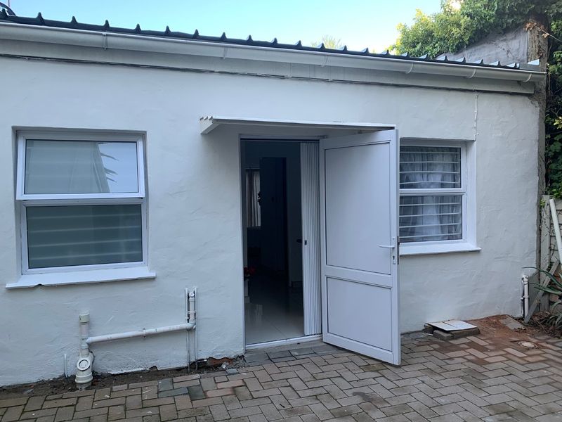 Rear exterior view of the apartment featuring a paved patio area, white rendered walls, and uPVC window frames with security bars.