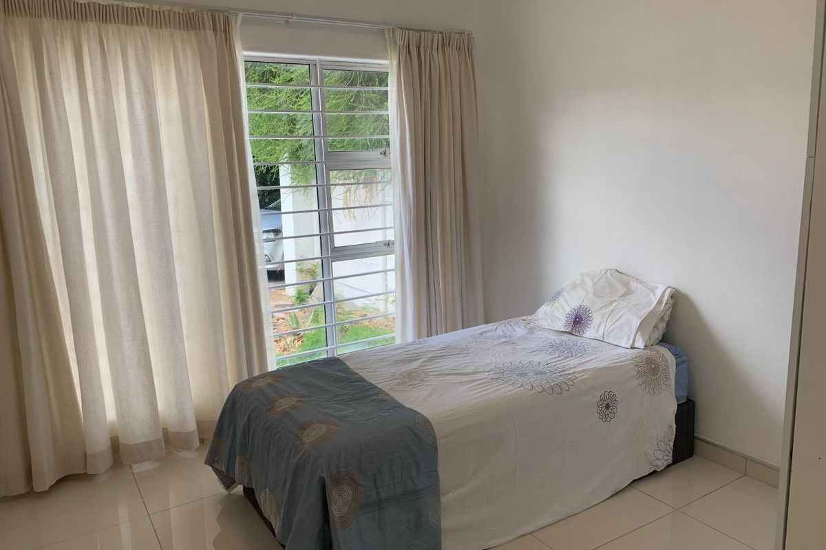 A simple bedroom featuring tiled flooring and a window fitted with security bars, providing natural light and a view of the exterior.