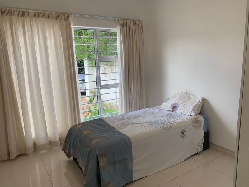 A simple bedroom featuring tiled flooring and a window fitted with security bars, providing natural light and a view of the exterior.