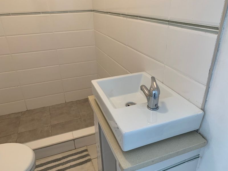 A compact bathroom featuring a modern vessel sink on a stone-topped vanity, complemented by white wall tiling and neutral floor tiles.