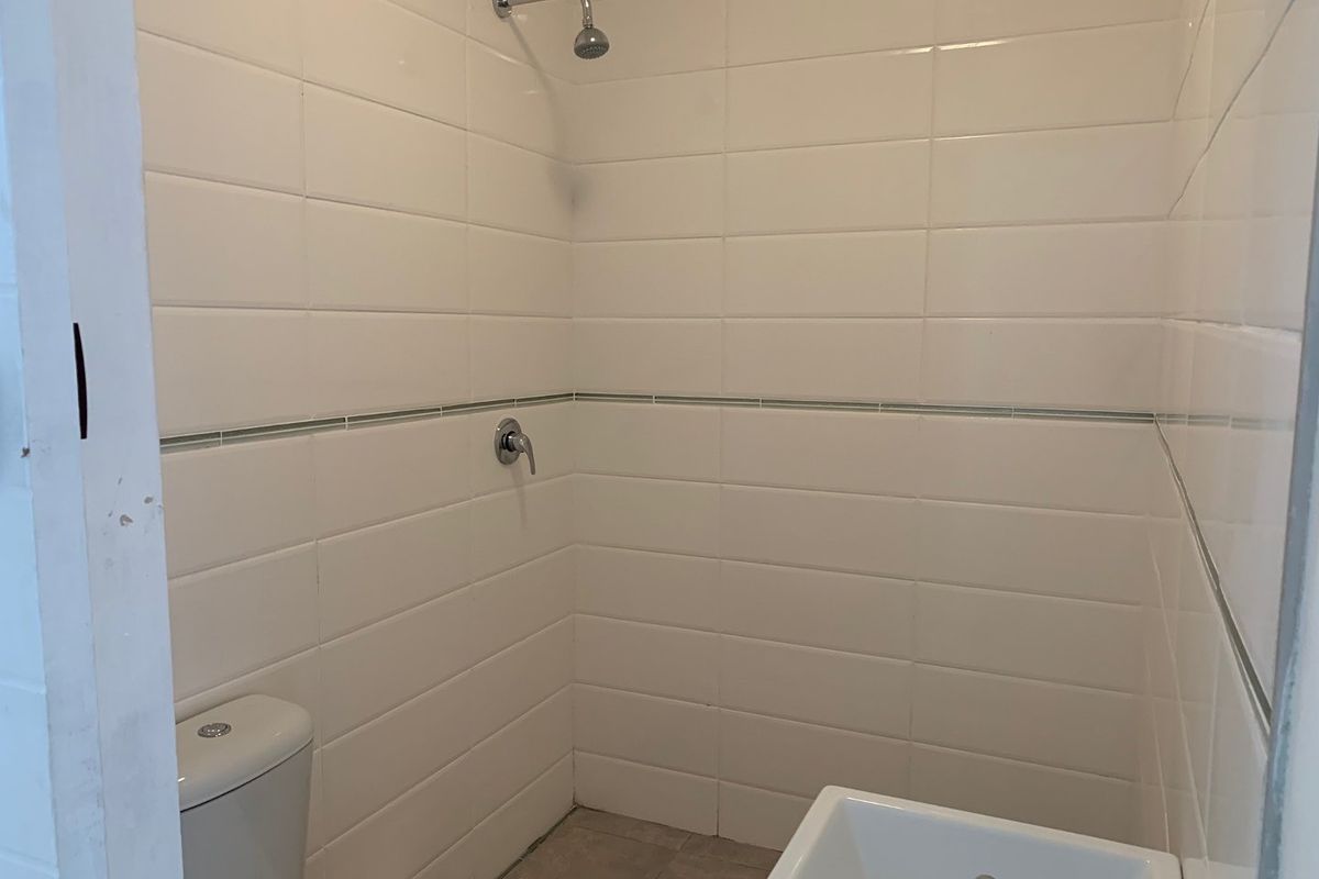 A functional bathroom featuring white wall tiles, a shower, a toilet, and a washbasin.