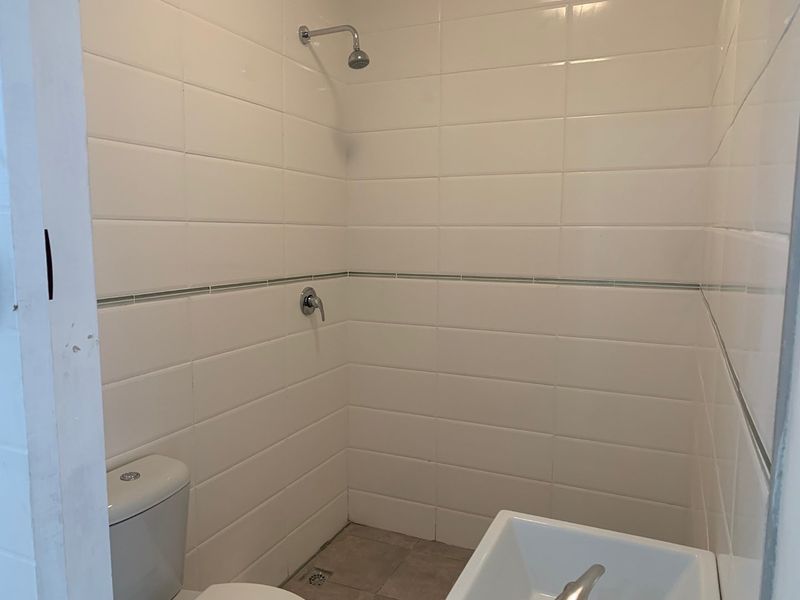 A functional bathroom featuring white wall tiles, a shower, a toilet, and a washbasin.