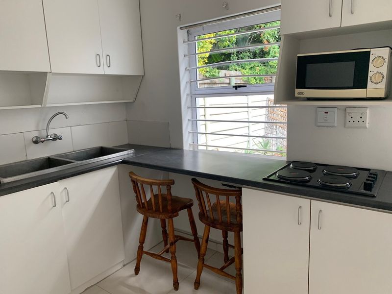Compact kitchen featuring white cabinetry, dark laminate countertops, a double basin sink, and a built-in electric hob with an integrated microwave shelf.