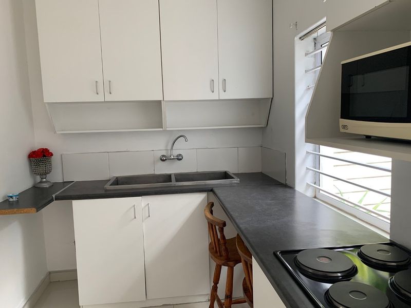 Compact kitchen featuring white cabinetry, dark laminate countertops, a double basin sink, and a built-in electric hob with microwave storage.
