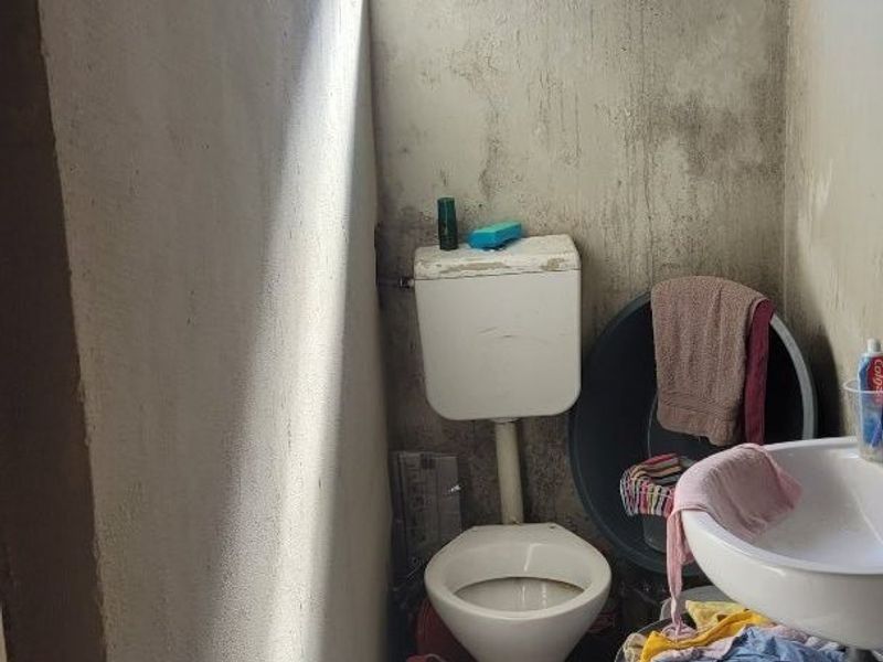 A small, dated bathroom featuring a standard toilet and pedestal basin, requiring significant renovation and wall surface repairs.