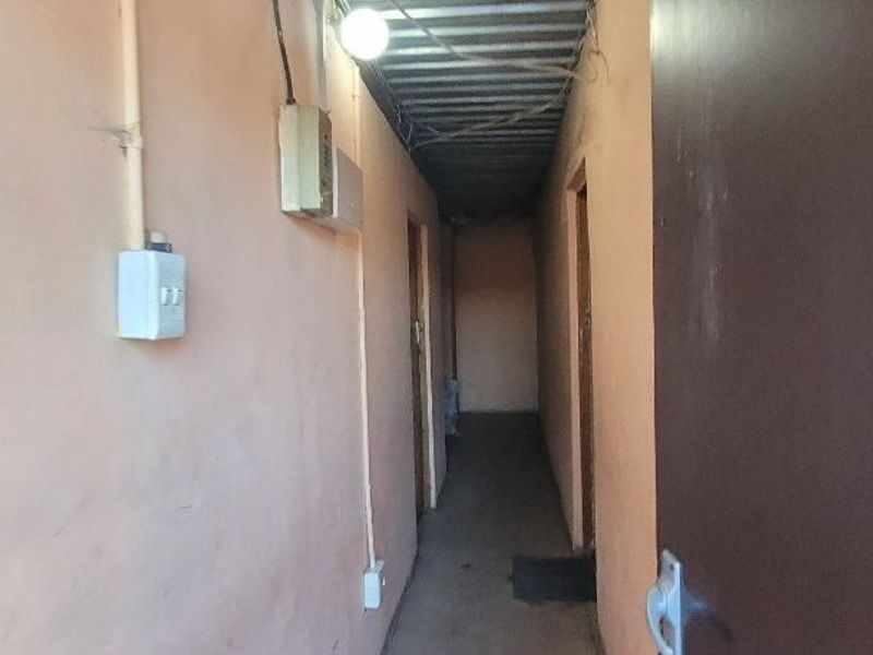 A narrow, utilitarian hallway featuring exposed electrical conduit, a corrugated metal ceiling, and basic wall finishes.