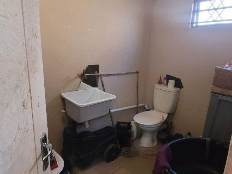 A small utility or laundry room featuring a basic utility sink, toilet, and exposed plumbing, requiring cosmetic updates and finish improvements.