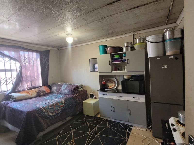 A compact bedroom featuring built-in cabinetry and security window bars, currently used as a multi-functional living space.