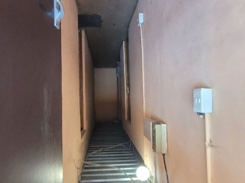 A narrow, utilitarian hallway or service passage featuring exposed electrical wiring and a metal staircase, requiring maintenance and cosmetic updates.