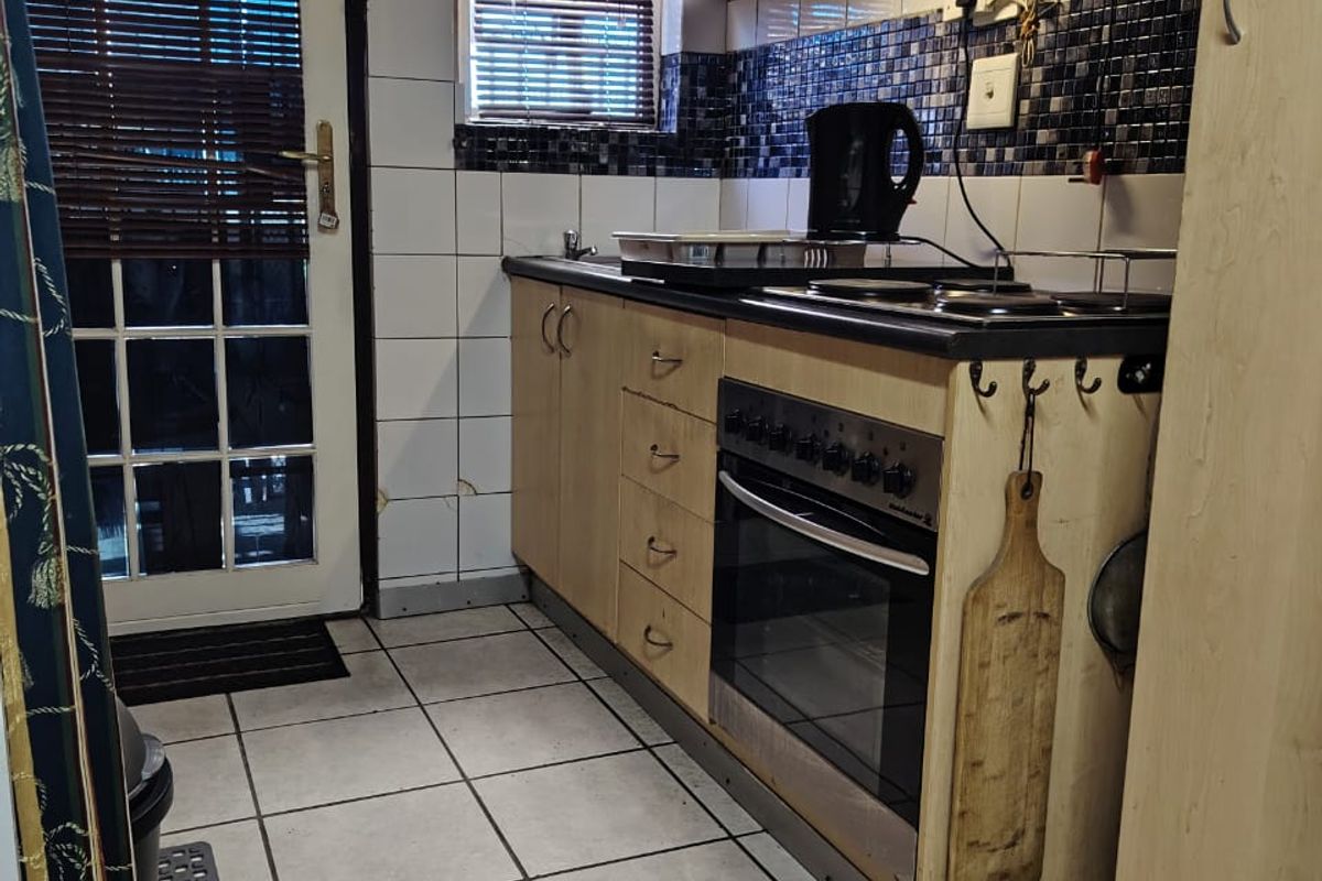 Compact kitchen featuring built-in cabinetry, electric oven, hob, extractor fan, and tiled finishes, with direct access to the exterior via a glass panel door.