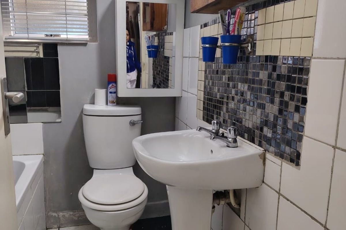 Compact bathroom featuring a pedestal basin, toilet, and bathtub with mosaic tile detailing. The space requires cosmetic updates to finishes and tiling.