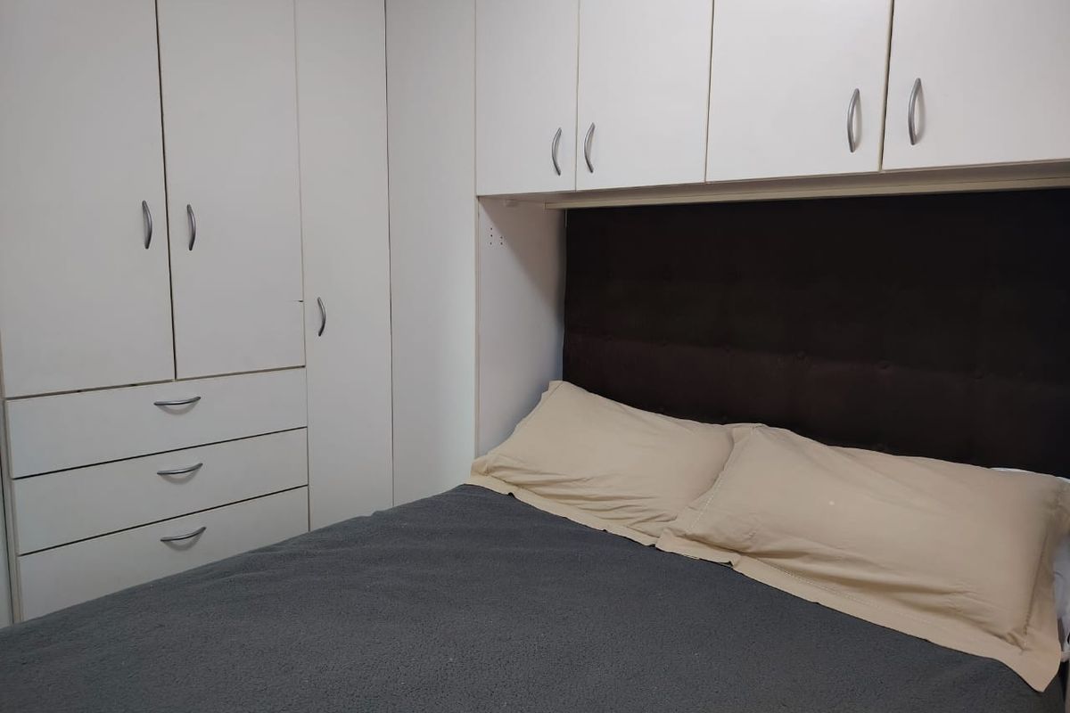 A bedroom featuring white built-in wardrobes and overhead storage cabinets with a dark upholstered headboard.