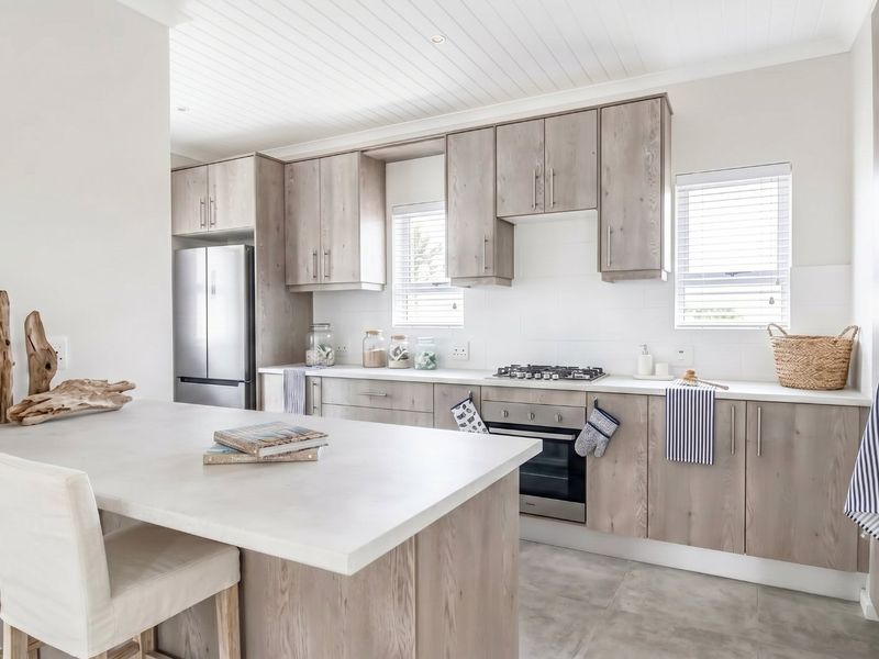 Modern kitchen featuring light wood cabinetry, stone countertops, a central island, and integrated appliances with a clean, contemporary aesthetic.