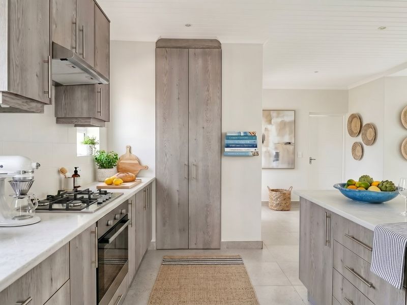 Modern kitchen featuring light wood-grain cabinetry, stone countertops, integrated gas cooktop, built-in oven, and a central island, finished with neutral tiled flooring.