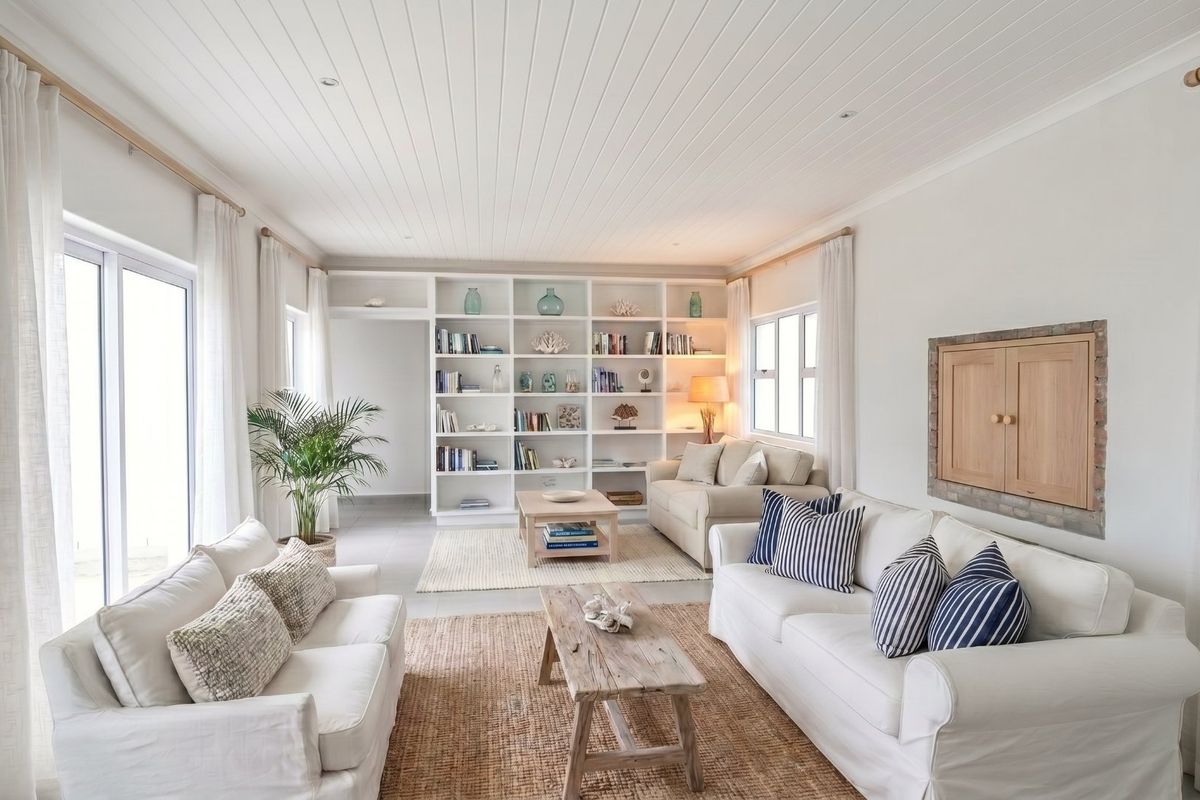 A bright and airy living room featuring built-in shelving, a tongue and groove ceiling, and large sliding glass doors providing ample natural light.