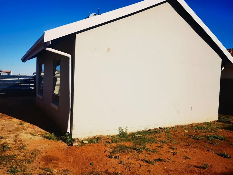 Side view of the property showing the exterior wall, guttering, and downpipe with unlandscaped ground area.