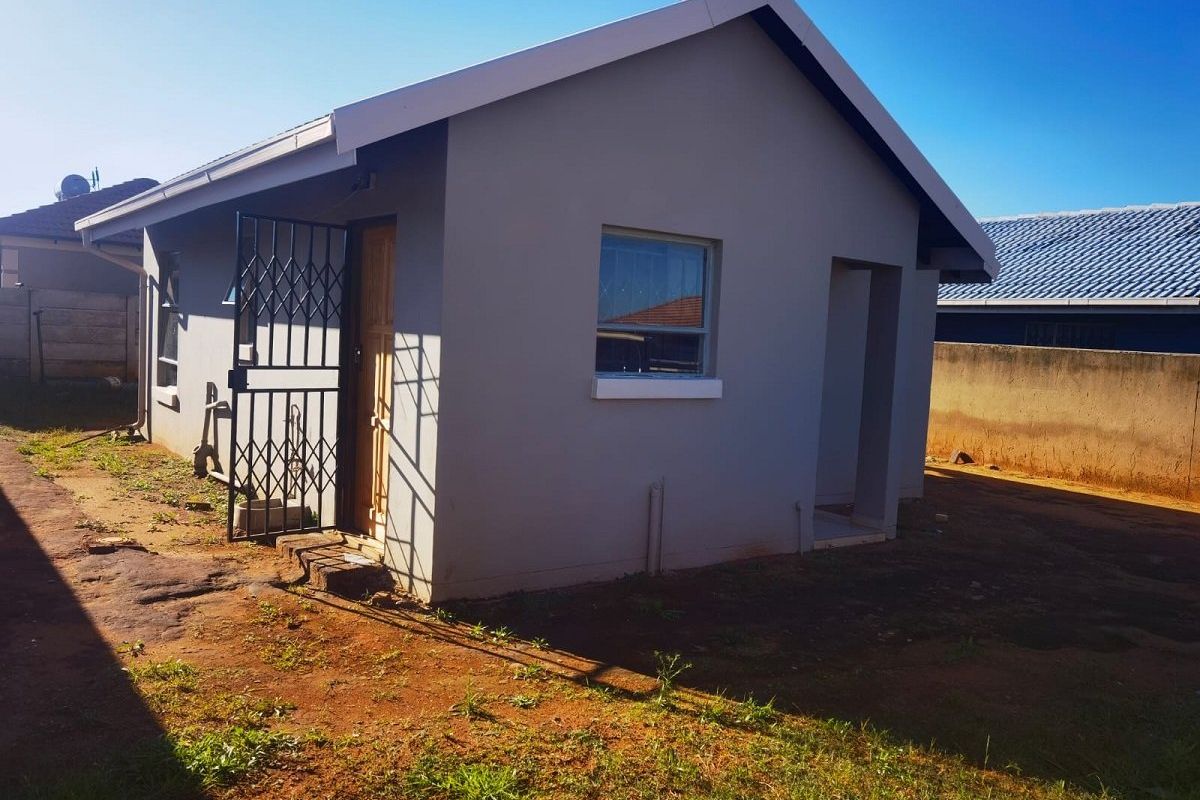 A view of the rear exterior of the house featuring plastered walls, a tiled roof, and a security gate entrance.