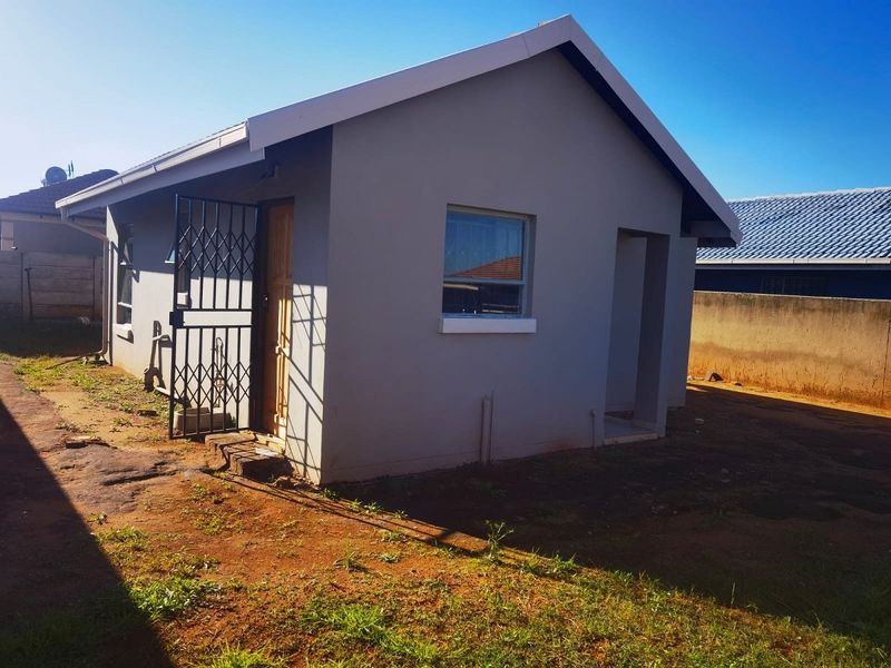 A view of the rear exterior of the house featuring plastered walls, a tiled roof, and a security gate entrance.