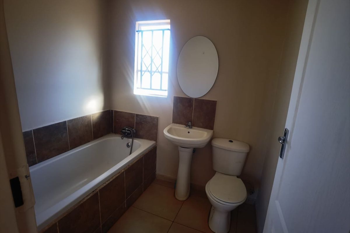 A functional bathroom featuring a bathtub, pedestal basin, and toilet with tiled splashbacks and natural light from a window with security bars.