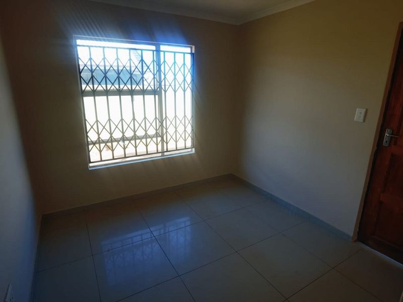 A clean, empty bedroom featuring neutral wall paint, tiled flooring, and a window fitted with a security gate.
