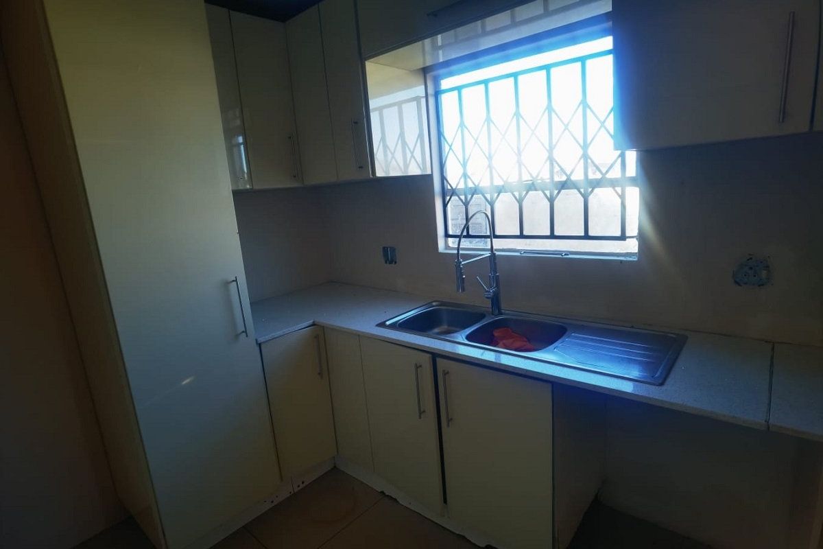 A functional kitchen space featuring built-in cabinetry, laminate countertops, and a stainless steel double sink with a window security gate.