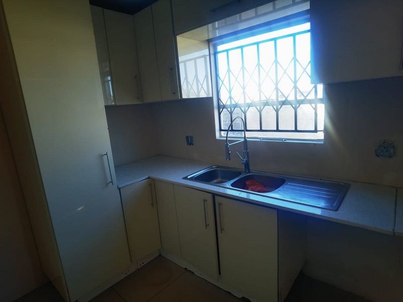 A functional kitchen space featuring built-in cabinetry, laminate countertops, and a stainless steel double sink with a window security gate.