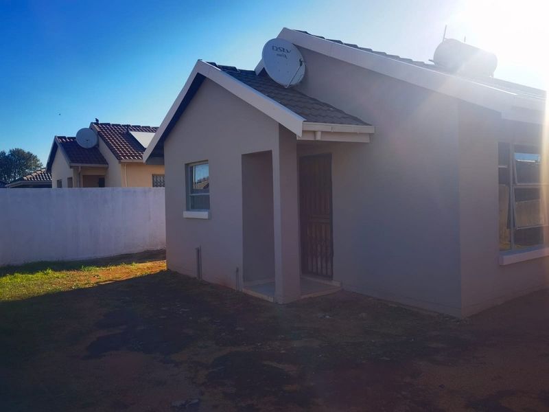 Rear view of a single-story residential house featuring a tiled roof, solar water heater, and security gate access.
