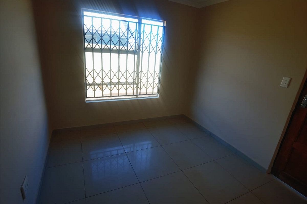 An empty bedroom featuring tiled flooring and a window fitted with a security gate.