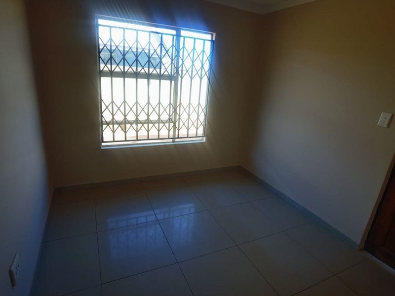 An empty bedroom featuring tiled flooring and a window fitted with a security gate.