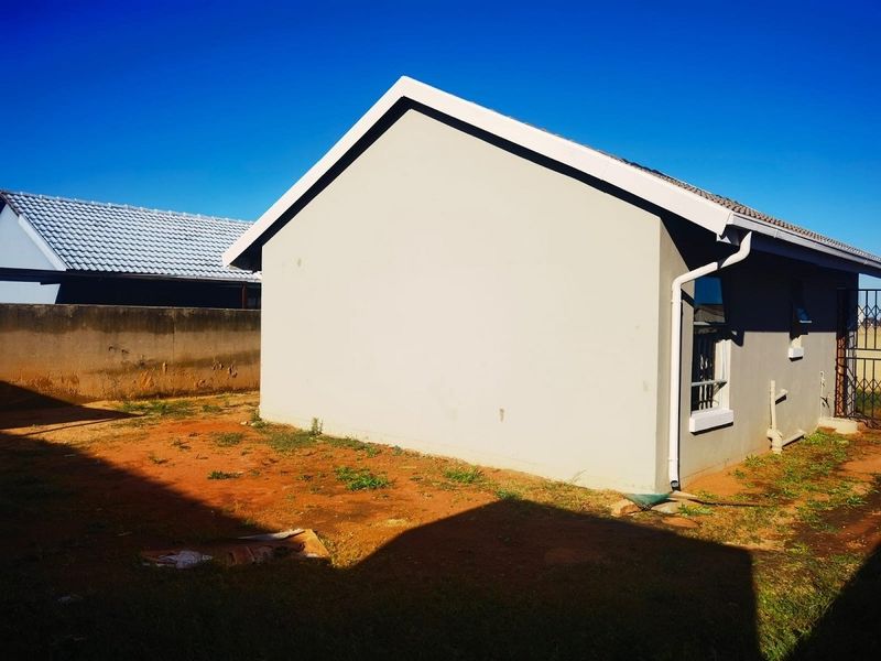 Rear view of the property showing the exterior wall, roofline, and surrounding unlandscaped yard area.