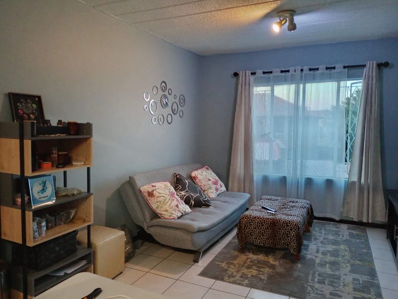A living room featuring tiled flooring, a large window with security bars, and a ceiling-mounted spotlight fixture.